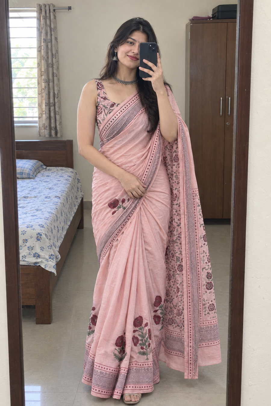 Woman wearing the pink saree taking a bedroom mirror selfie